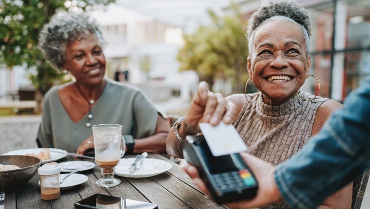 Two women sitting outside at a table. One holds their credit card to pay.